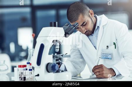 Focused male lab technician using digital tablet working on medical development and innovation project with microscope, taking notes. Doctor Stock Photo