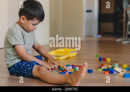 Boy building a tower of cubes, sitting on the floor at home. Concept of children development, education and creativity at home. Stock Photo