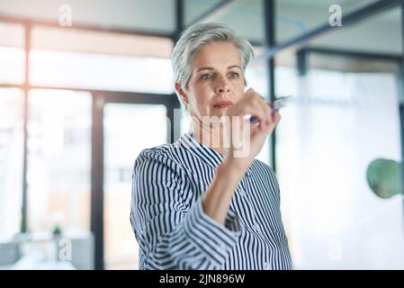 Just make sure you always take note. a mature businesswoman writing down notes on a glass wall in her office. Stock Photo