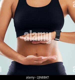 Maintain a balance between regular exercise and healthy eating. Studio shot of an unrecognizable sporty woman framing her stomach with her hands Stock Photo