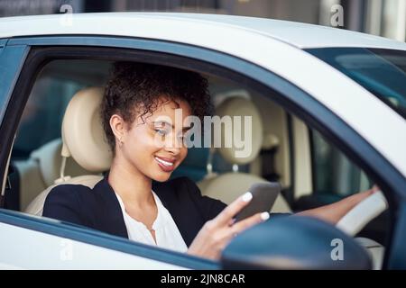 Letting her friends know shes got four wheels now. an attractive young businesswoman using a smartphone while driving her car. Stock Photo