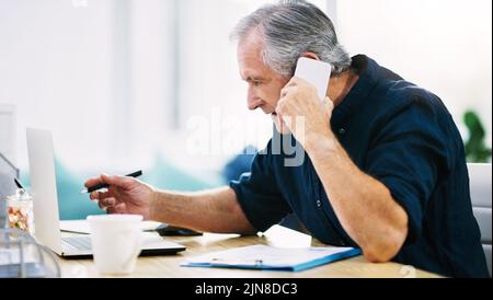 Hes having a busy day at the office today. a mature businessman writing a few notes down while answering a phone call in his office. Stock Photo