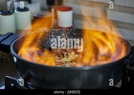 Beef meat fried with onions in frying pan, flambe on gas stove Stock Photo