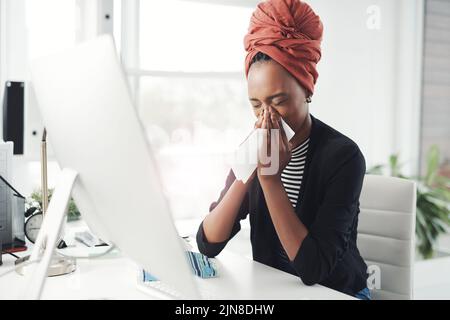 She cant afford to be sick right now. an attractive young businesswoman blowing her nose while working at her desk in the office. Stock Photo