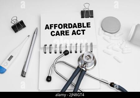 Medicine concept. On the table are a stethoscope, pills, a thermometer and a notebook with the inscription - affordable care act Stock Photo