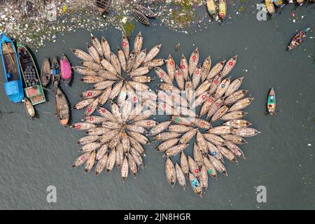 Dhaka, Bangladesh. 9th Aug, 2022. View from above of hundreds of wooden boats resemble like flowers in Dhaka River Port, as they fan out around their moorings. The boats, decorated with colourful patterned rugs, are ready to transport workers from the outskirts of the city to their jobs in the centre. The Buriganga river is used as a route into Dhaka city for millions of workers every day. (Credit Image: © Mustasinur Rahman Alvi/ZUMA Press Wire) Stock Photo