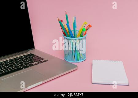 Laptop pens and colored pencils in blue stand and white stickers on pink background, back to school and business education concept Stock Photo