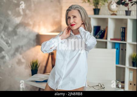 A woman standing in the office, feeling bad and looking tired Stock Photo