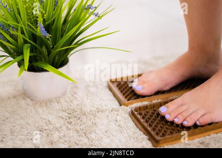 yogi woman stand on wooden sadhu board with sharp nails. Green plant in white pot near. Concept alternative medicine Stock Photo