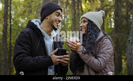 Young happy hispanic couple in love close-up standing hugging outdoors in cold weather drinking hot tea in nature tourists resting on hike recuperate Stock Photo