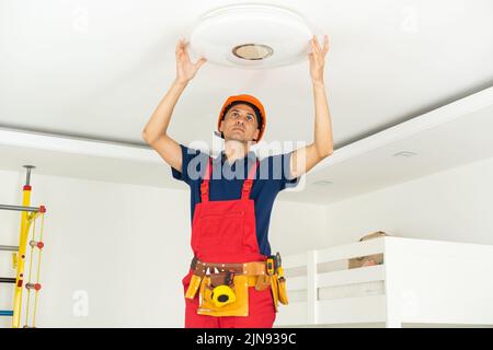 young man repairing cable wiring and installs or replaces the halogen lamp on the ceiling. Stock Photo