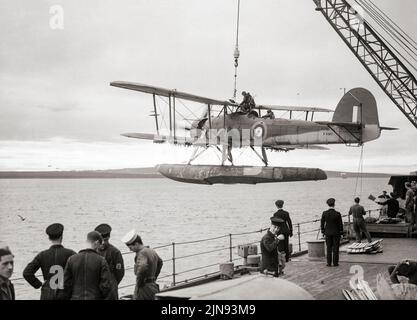 After a reconnaissance flight, a Fairey Swordfish sea plane returns to HMS Malaya and is hoisted in board. Despite being obsolete by 1939, the Swordfish achieved some spectacular successes during the war. Notable events included the famous attack on the German battleship Bismarck, which contributed to her eventual demise. The Swordfish sank a greater tonnage of Axis shipping than any other Allied aircraft during the war and remained in front-line service until V-E Day, having outlived some of the aircraft intended to replace it.