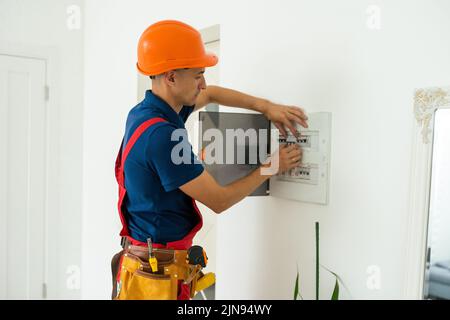 Young adult electrician builder engineer inspecting electric counter equipment in distribution fuse box Stock Photo