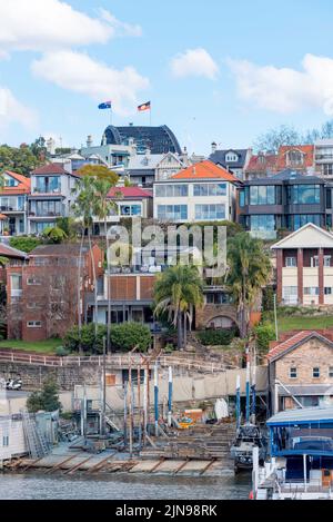 The flags and arch of the Sydney Harbour Bridge peak over the hill behind houses in Kirribilli and Sydney Harbour Slipways Pty Ltd on Careening Cove Stock Photo
