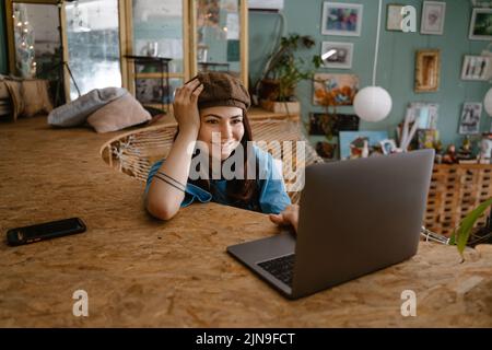 Young woman artist using laptop while resting in hammock at her studio indoors Stock Photo