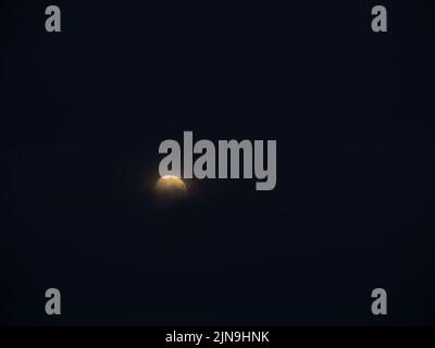 Moon, part obscured by cloud, hangs in starless night sky. Mystical in the darkness. Stock Photo