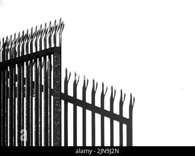 Spiked and barbed metal gate in fence with shadow. Security concept, background. Stock Photo