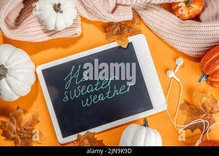 Cozy fall background with tablet, ear-pods, white, orange pumpkins, autumn leaves decor on high-colored orange background. Autumn still life compositi Stock Photo