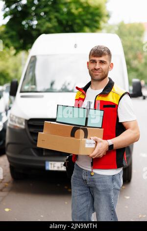 Man standing in front of a minibus working for a delivery service holding packages to be delivered Stock Photo