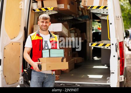 The happy courier in front of the work car has taken the packages and is ready to deliver them Stock Photo