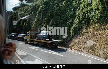 Broken down Fiat 126 on the back of a recovery truck in Italy viewed from a coach window with copy space and foreground detail. Stock Photo