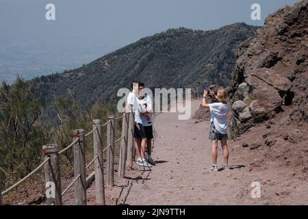 A mum and two sons pose for a family phone picture on the walkway at the top of Mount Vesuvius Italy looking out to the view towards Naples. Stock Photo
