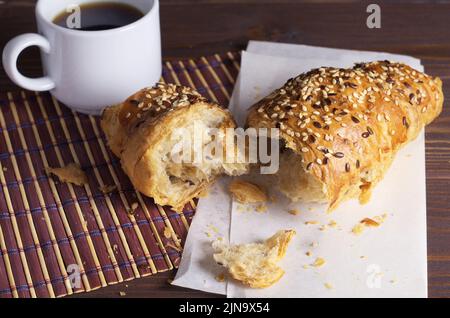 Broken croissant with seeds of flax and cup of black coffee on table close up Stock Photo