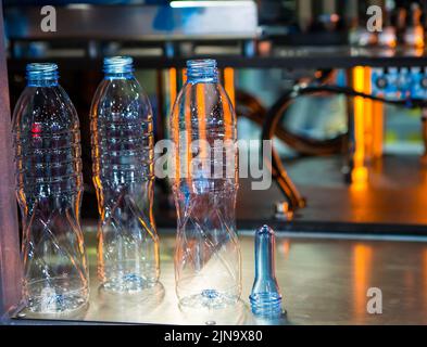 Plastic bottles and raw material for plastic bottle manufacturing process on plastic bottle blowing machine. Stock Photo