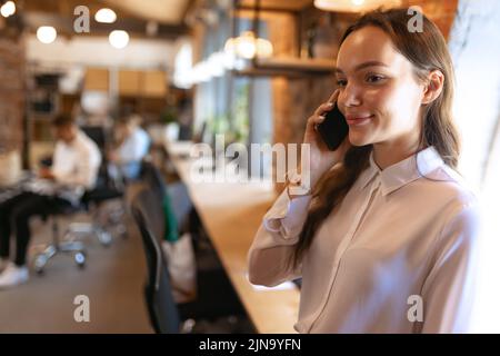 Young charming smiling woman at loft style office with group of colleagues in background. Concept of success, business, career, achievements Stock Photo