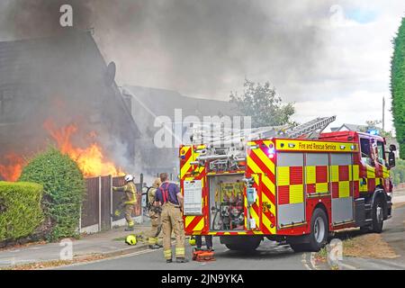 Fire engine tender Essex Fire and Rescue Service fire brigade firemen firefighters at burning house fire ablaze flames black smoke close up England UK Stock Photo