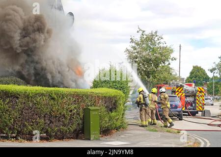 Essex Fire and Rescue Service fire engine & group of fire brigade firemen firefighters spraying water jet on house fire smoke and flames   England UK Stock Photo