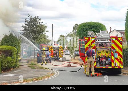 Firemen spraying water jet on house two fire brigade engines & firefighters Essex Fire and Rescue Service in residential street scene England UK Stock Photo