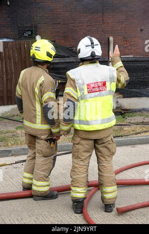 Back view Essex Fire and Rescue Service fire brigade fireman firefighter house building fire with incident commander blaze under control aftermath UK Stock Photo