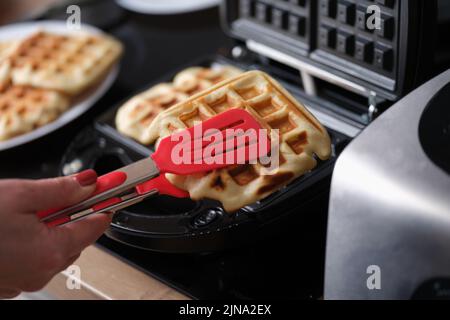Pastry chef takes hot waffles from waffle iron in kitchen Stock Photo