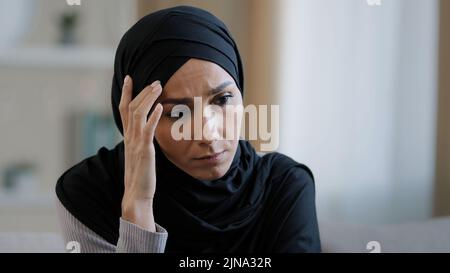 Upset sad girl in hijab sit alone get bad news feel depressed frustrated muslim woman suffering from illness worried about unresolved problems feeling Stock Photo