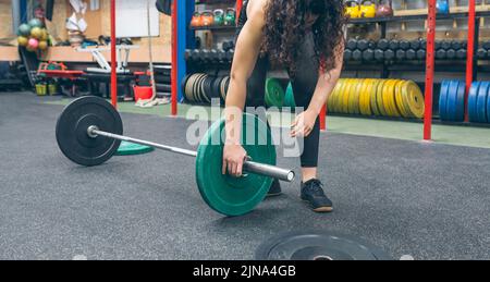 Woman crouching changing the discs of the weightlifting bar Stock Photo