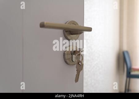Close-up of a metal handle with a key inserted into the keyhole on an open white wooden door Stock Photo