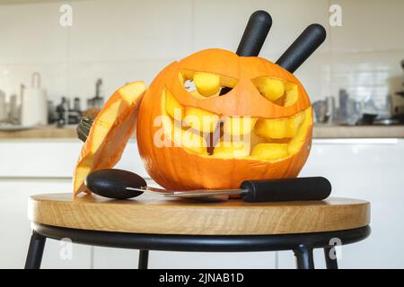 Carved Halloween pumpkin, jack lantern (Jack-o'-lantern), with carving tools. Spooky laughing, scary head. Stock Photo