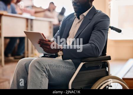 Close-up of African teacher with disability sitting on wheelchair and using digital tablet during lecture Stock Photo