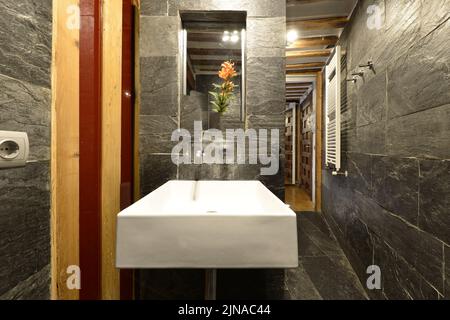 Bathroom with black slate tiles and floors, wall-mounted mirror and square white porcelain sink Stock Photo