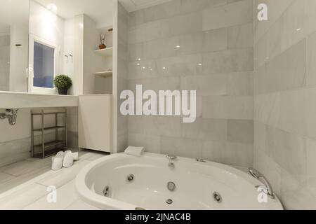 Hydromassage bathtub in a bathroom with white marble tiling and a large countertop with matching sink Stock Photo