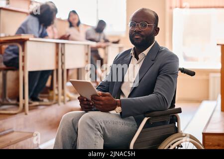 Portrait of African teacher with disability sitting on wheelchair using digital tablet at lecture at university Stock Photo