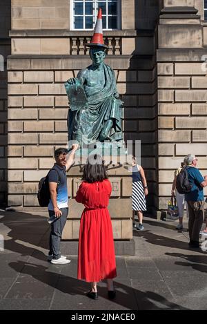 A tourist rubs the toe on the statue of the Scottish Philosopher David Hume, with traffic cone, on Edinburgh's Royal Mile.