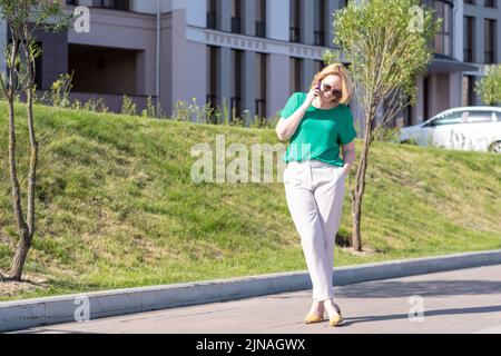Portrait of young student girl in glasses standing outdoors and talking on cell phone. Girl is walking along city street and calling her friends. Blur Stock Photo