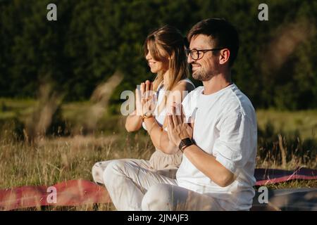 Young Adult Couple Meditating Outdoors in the Nature, Cheerful Woman and Happy Man Practicing Yoga Stock Photo