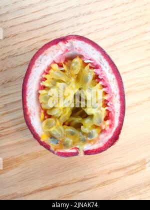 Half passion fruit showing yellow seeds and pink skin lying on wooden table Stock Photo