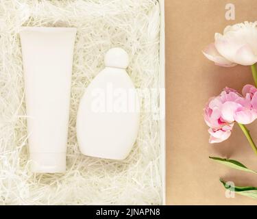 Beauty care, holiday composition with gift, white box with cosmetics product bottle and tube on a craft background with pink peonies. Cosmetic mockup Stock Photo