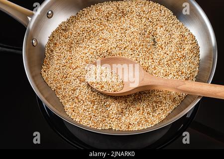 Sesame seeds toasting in a stainless steel frying pan. Roasting white til in a skillet. Organic benne grains in asian cuisine. Sesamum indicum crop. Stock Photo