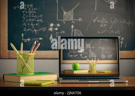 School supplies with digital laptop on wooden table with a blackboard on background Stock Photo