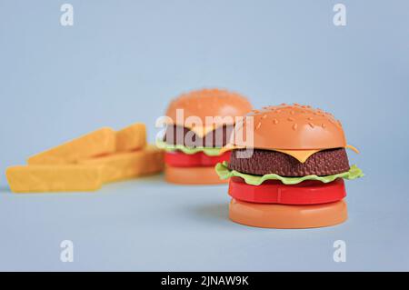 Plastic childrens toy burger with salad, tomato, meat and French fries on blue. Concept of harmful artificial food. Unhealthy. Not organic. Not useful Stock Photo